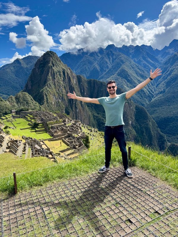 Arms wide in front of Machu Picchu and the green peaks behind it